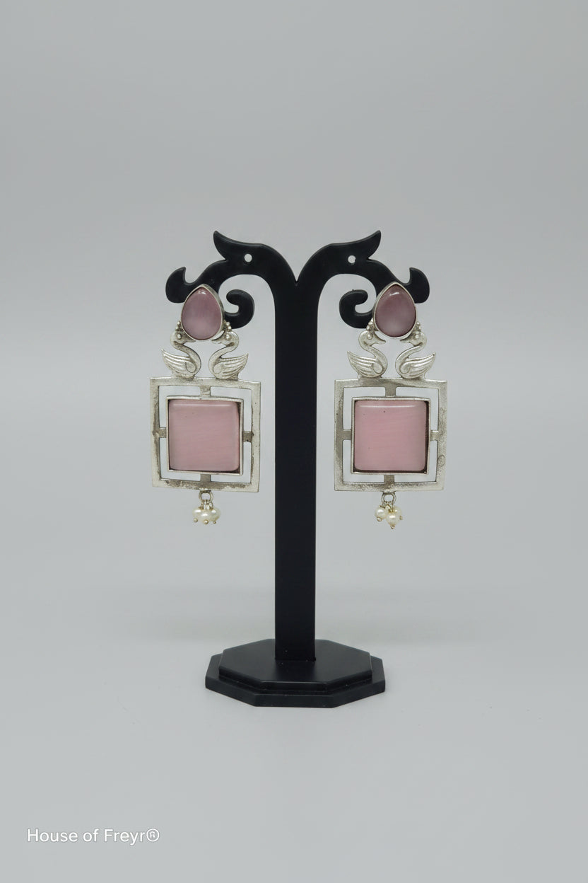 A pair of square-shaped dangler oxidised earrings with a silver-tone frame, baby pink center gemstone, and pearl accents.