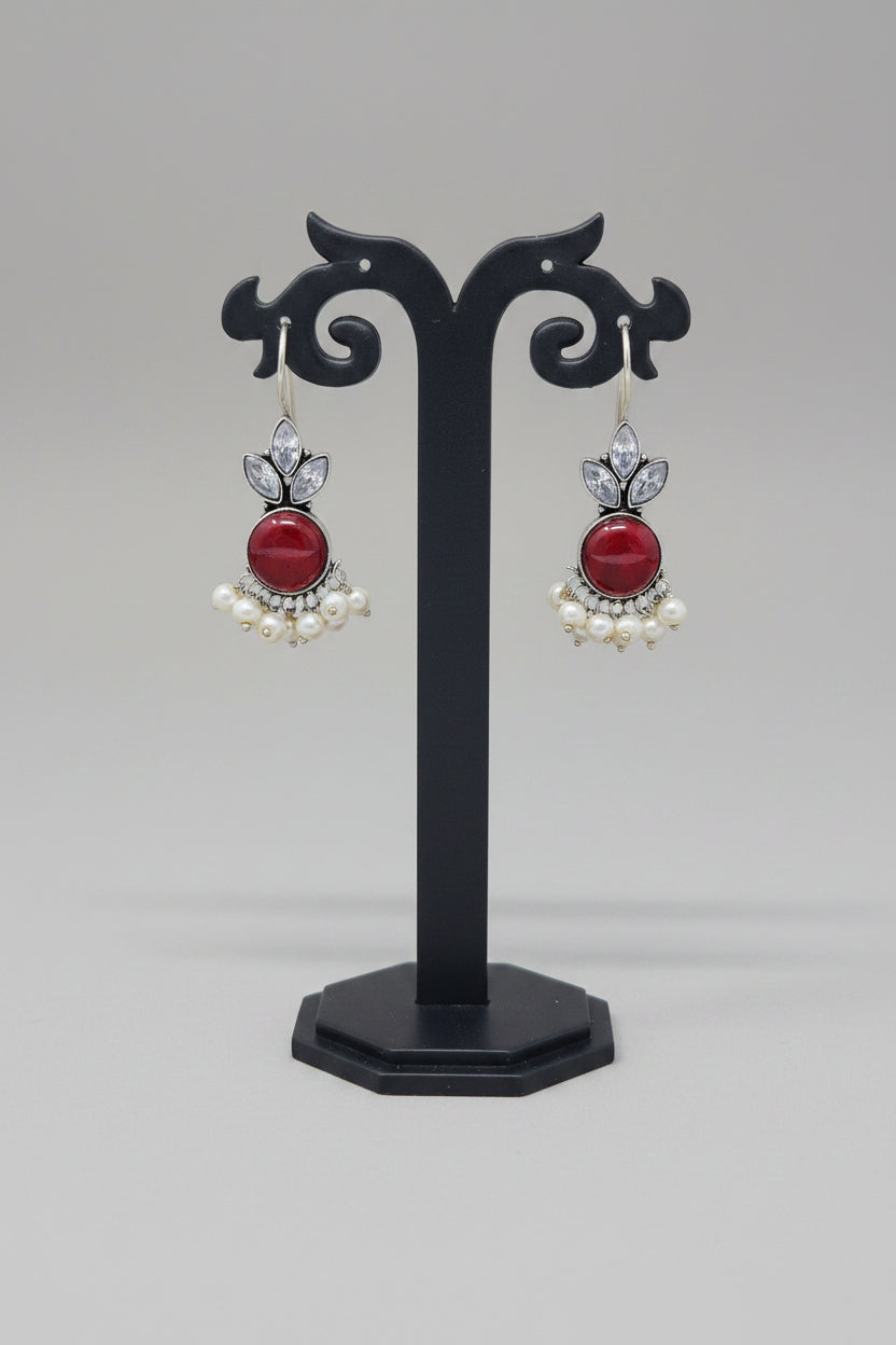 Oxidized silver hook earrings with a floral motif, pearl dangles. The earrings are adorned with a large red semi-precious stone and smaller crystal-like stones.
