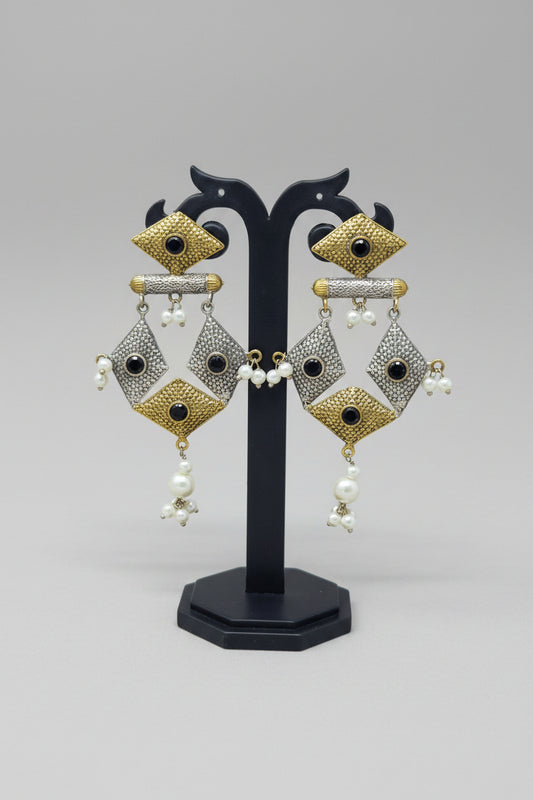 A pair of dual-tone geometric dangler earrings with black stone embellishments and pearl dangles.