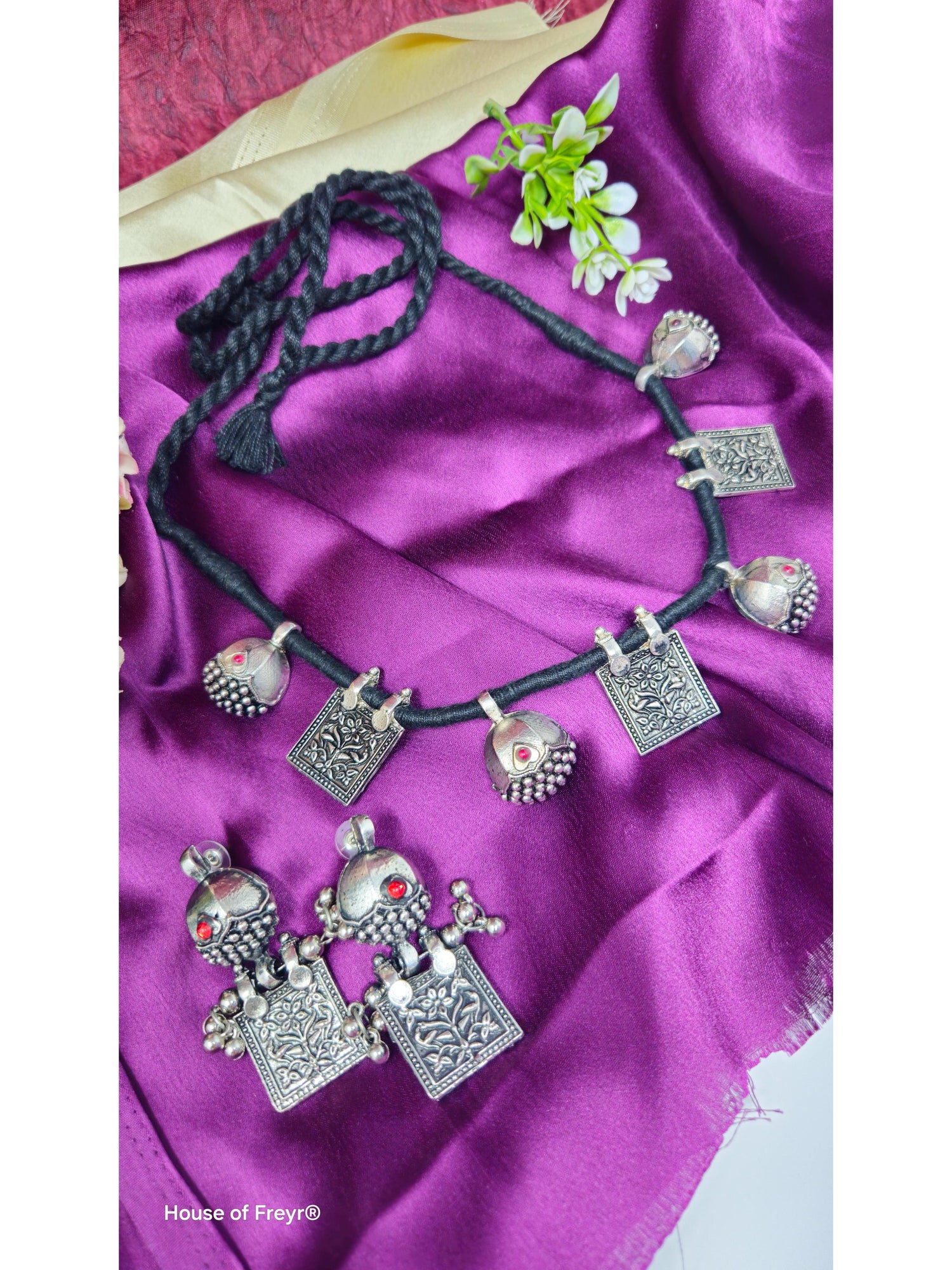 Silver necklace with decorative pendants on a purple fabric background