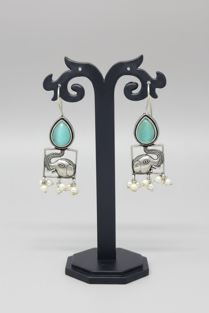 A pair of oxidised silver hook earrings featuring elephant motifs with teardrop-shaped blue semi-precious stones and pearl dangles.