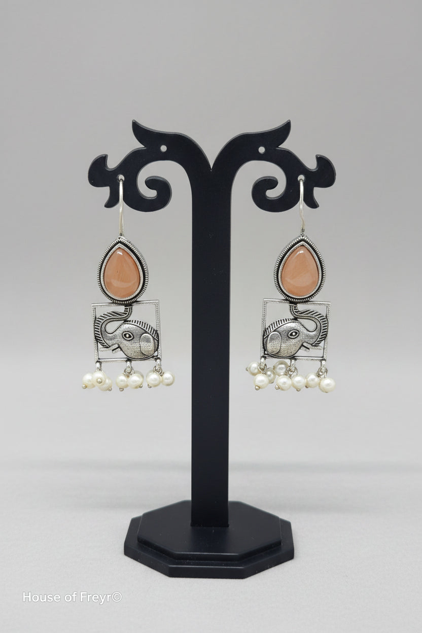 A pair of oxidised silver hook earrings featuring elephant motifs with teardrop-shaped peach semi-precious stones and pearl dangles.