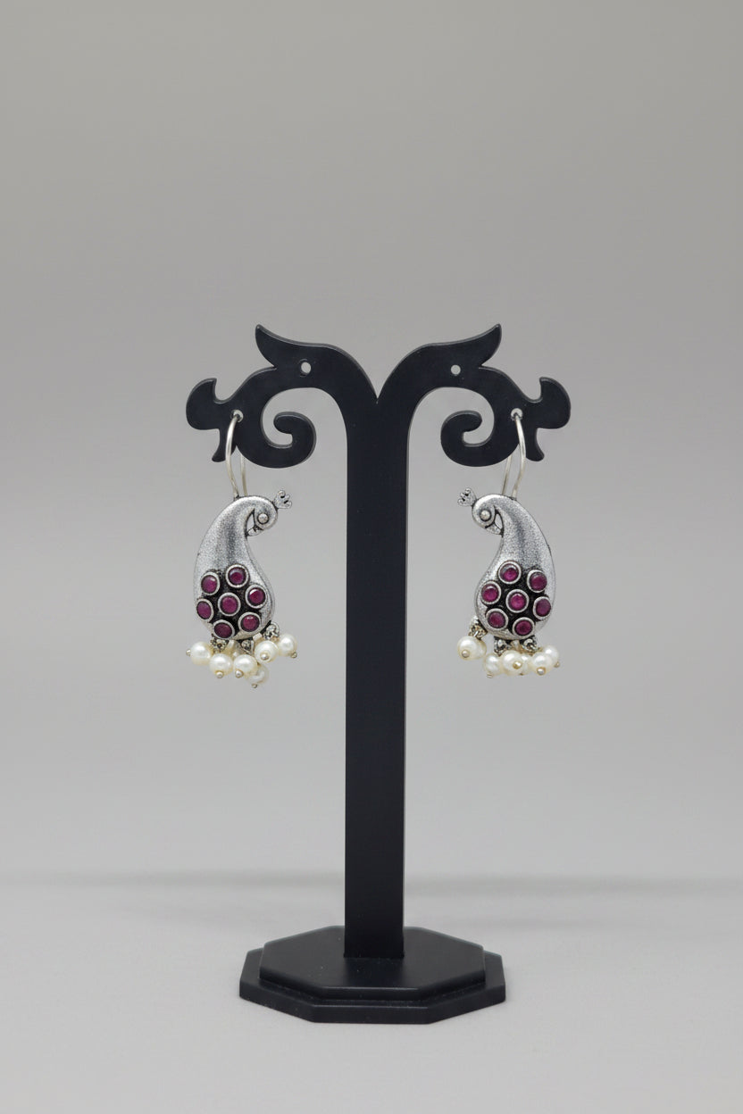 Premium oxidised antique silver peacock hook earrings with red colored stone accents and pearl drops.
