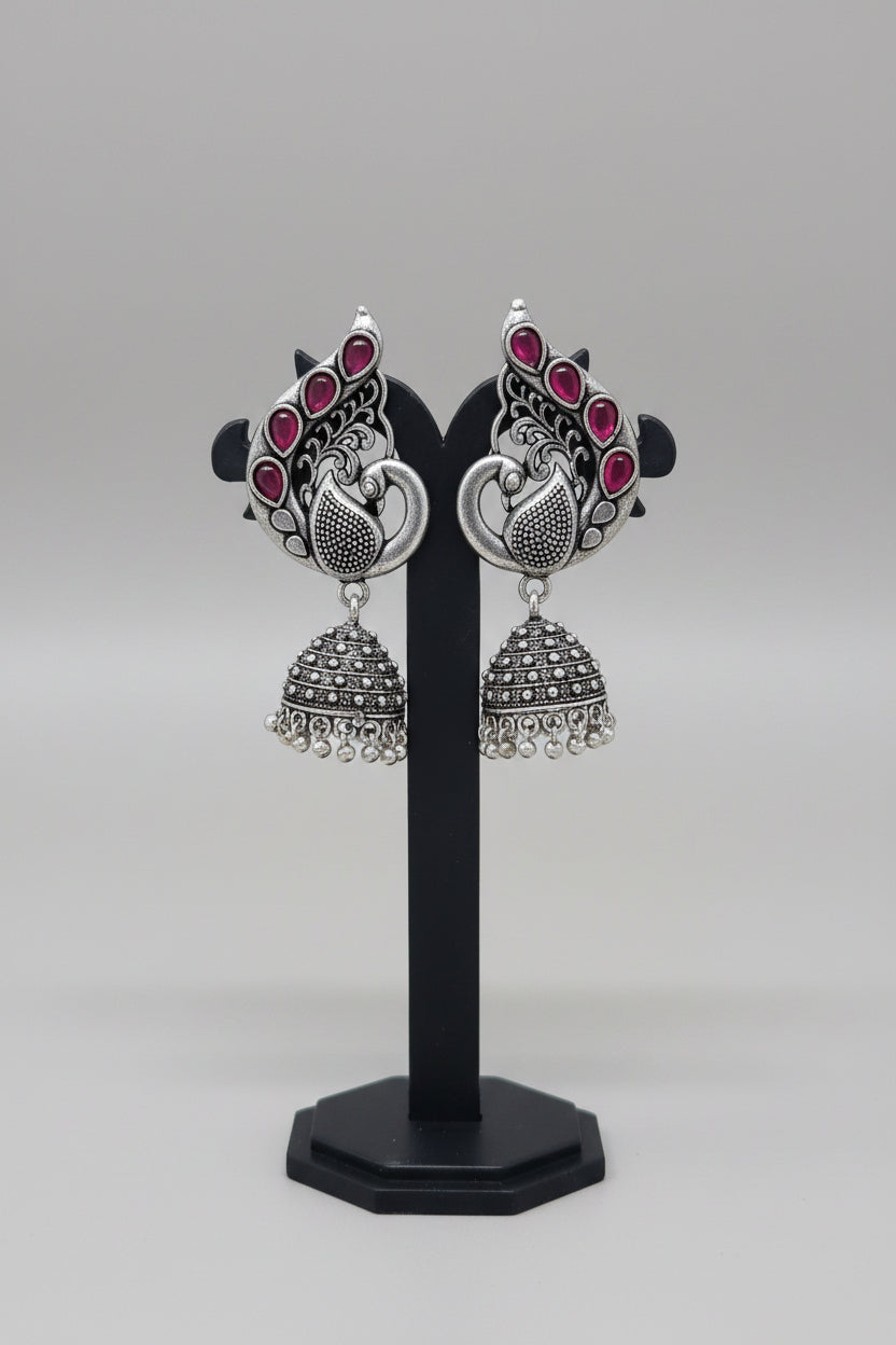Pair of oxidised silver jhumka earrings, peacock motif with red gemstones.