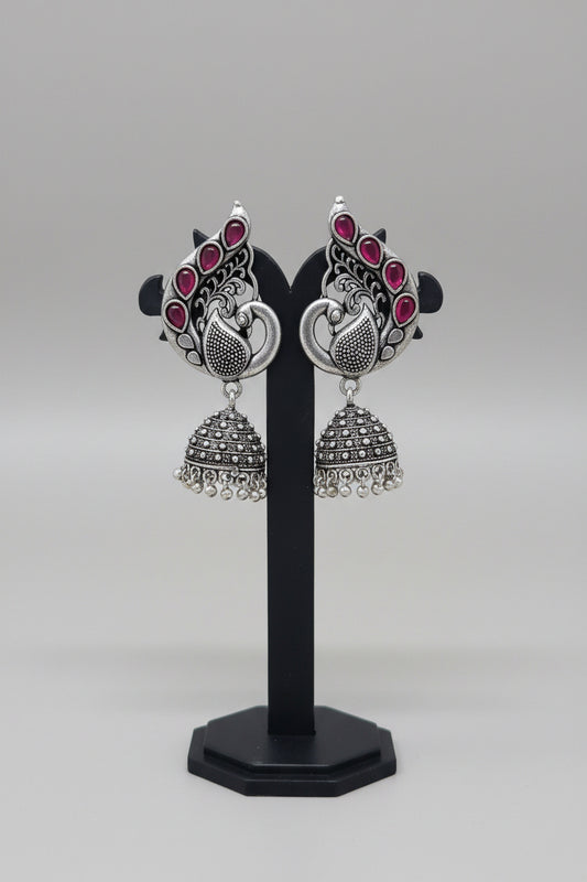 Pair of oxidised silver jhumka earrings, peacock motif with red gemstones.