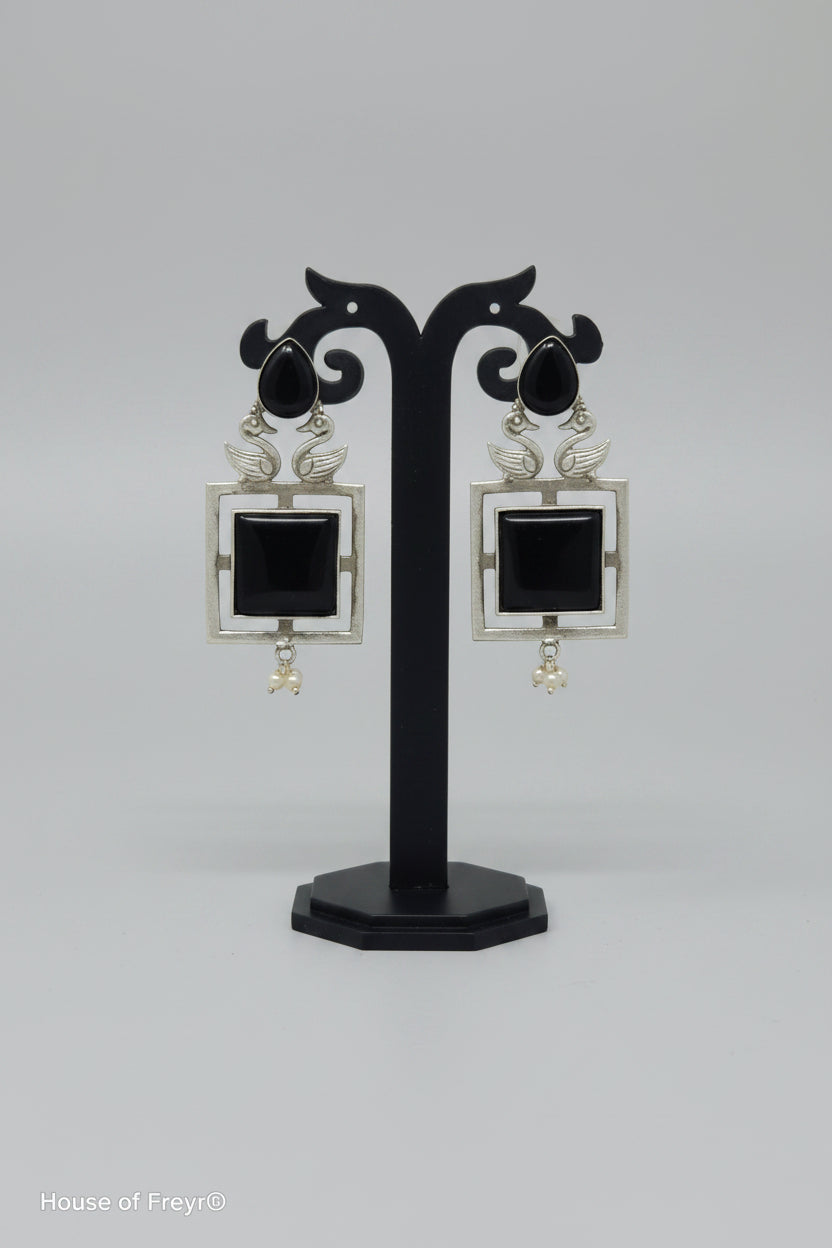 A pair of square-shaped dangler oxidised earrings with a silver-tone frame, black center stone, and pearl accents.