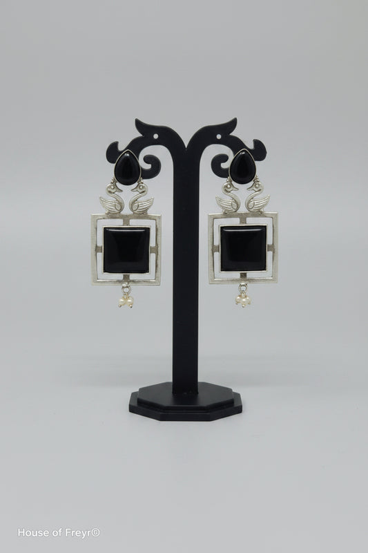 A pair of square-shaped dangler oxidised earrings with a silver-tone frame, black center stone, and pearl accents.