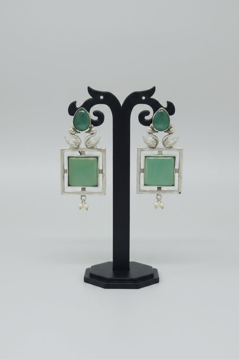 A pair of square-shaped dangler oxidised earrings with a silver-tone frame, cool mint center gemstone, and pearl accents.