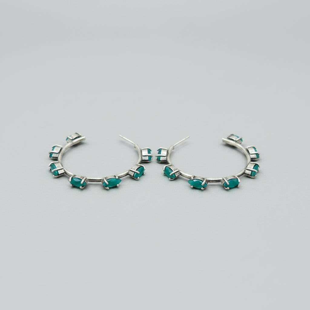 Pair of vintage oxidised silver hoop earrings with green stones on a light gray background
