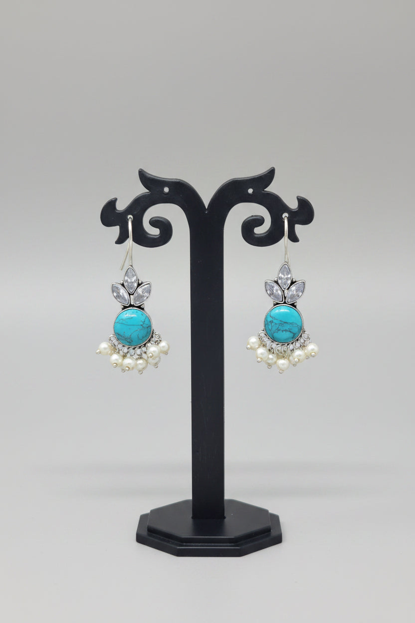  Oxidized silver hook earrings with a floral motif, pearl dangles. The earrings are adorned with a large turquoise semi-precious stone and smaller crystal-like stones.
