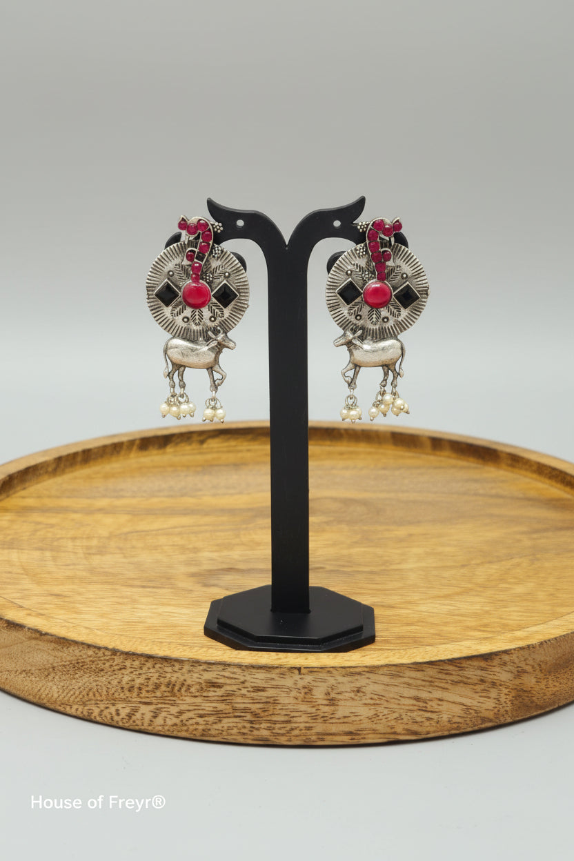 A pair of oxidized silver earrings with a tribal-inspired Nandi design, featuring red and black colored semi-precious stones and dangling pearls.